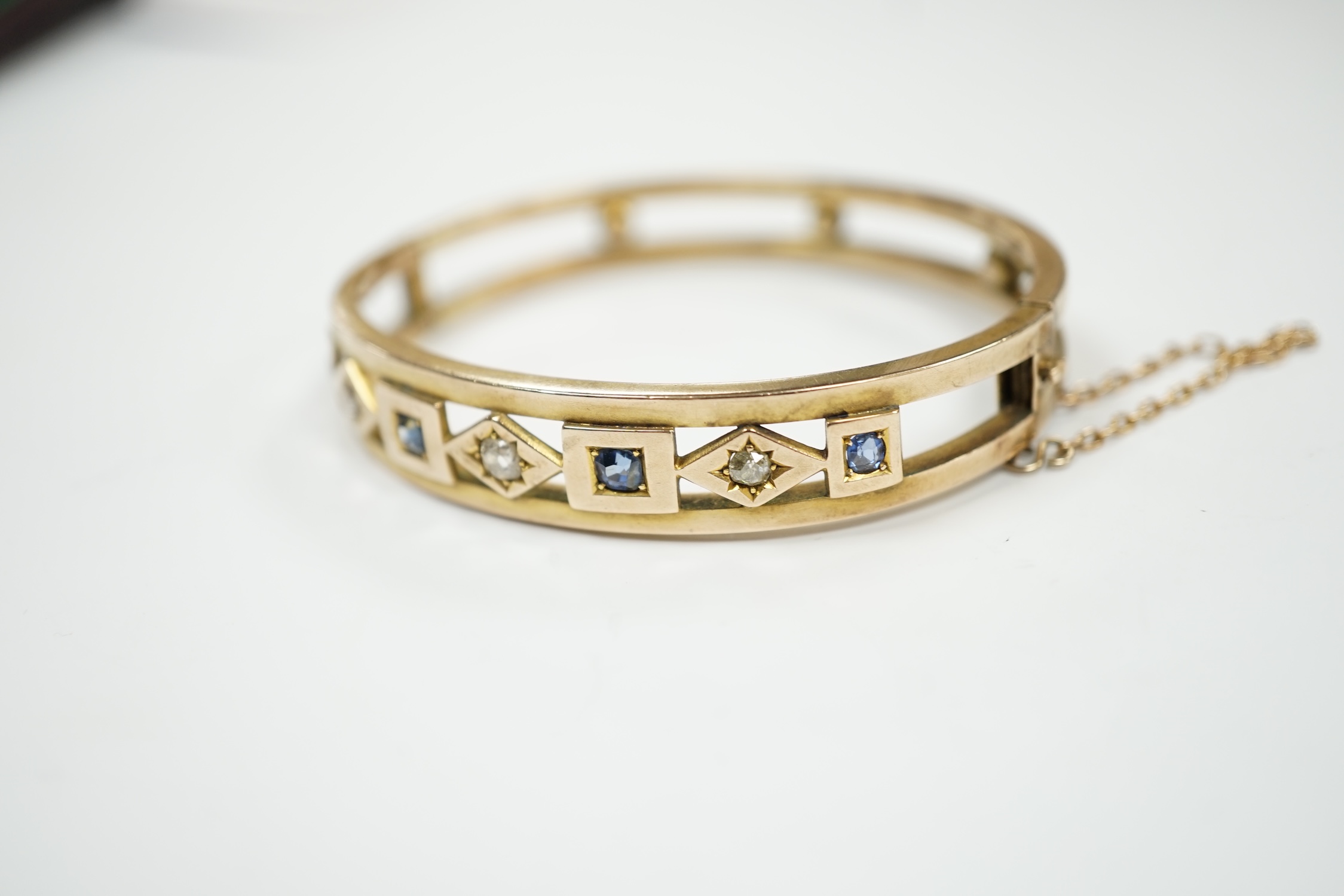 An Edwardian yellow metal, sapphire and diamond set hinged bangle, interior diameter 55mm, gross weight 14.4 grams, with box.